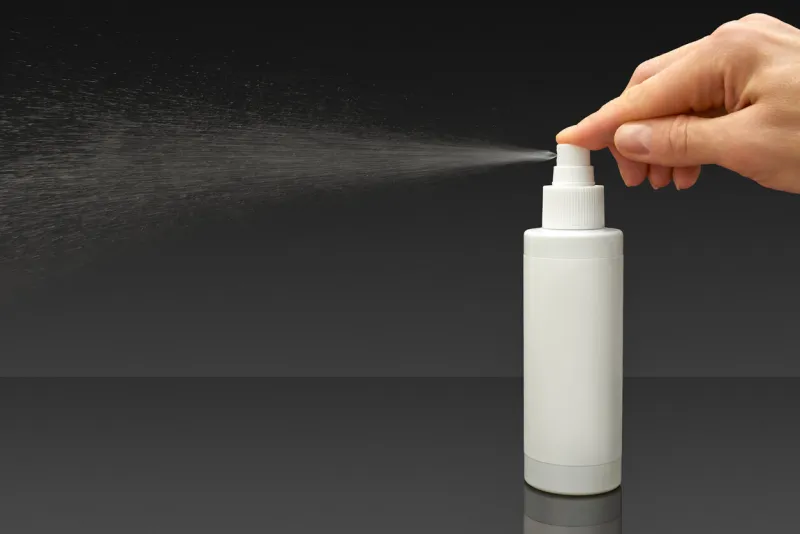 human hand and white cosmetic bottle spraying liquid, on black background