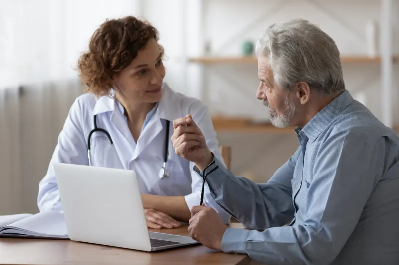 serious middle aged retired man consulting with young female physician doctor at checkup meeting in hospital skilled general practitioner giving healthcare medical advices to mature patient