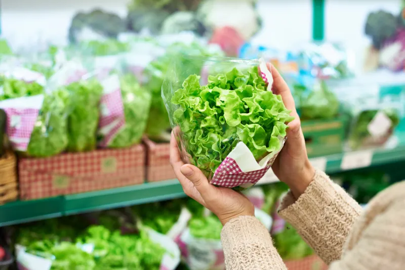 woman chooses a green leaf salad in the grocery store