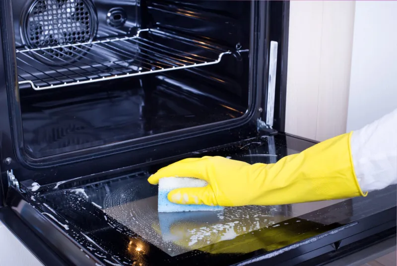 close up of female hand with yellow protective gloves cleaning oven door