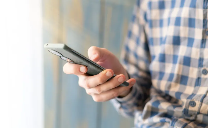 close-up image of male hands using smartphone at night on city shopping street, searching or social networks concept
