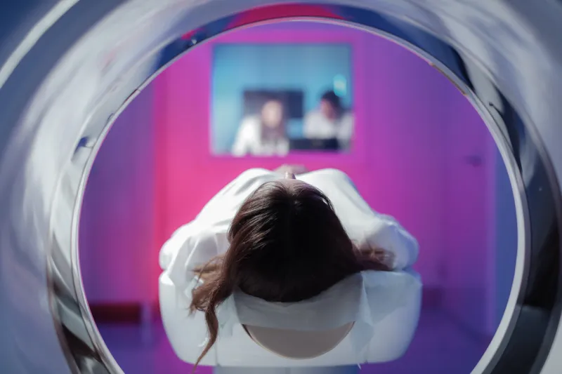 the girl patient is lying in the tomograph and waiting for a scan three doctors from the exam room look at the pictures