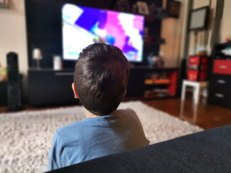 back view of kid watching tv while relaxing in the living room