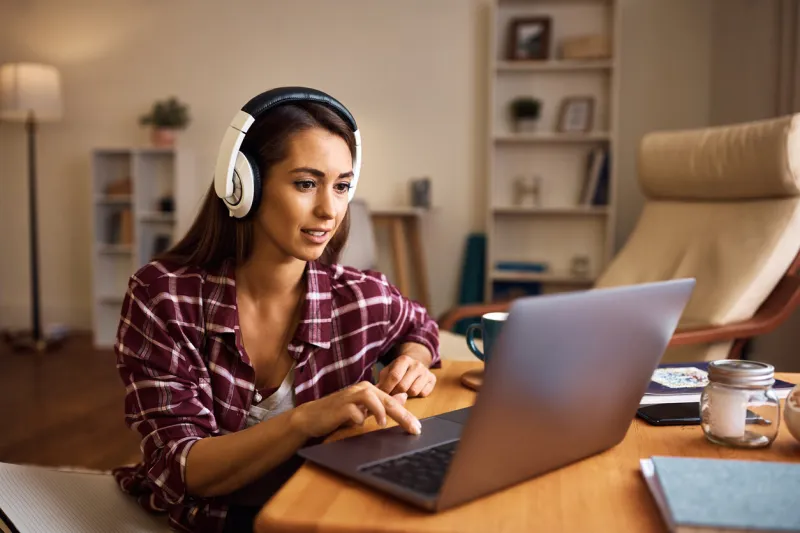 young woman with headphones using laptop while learning for upcoming exams at home