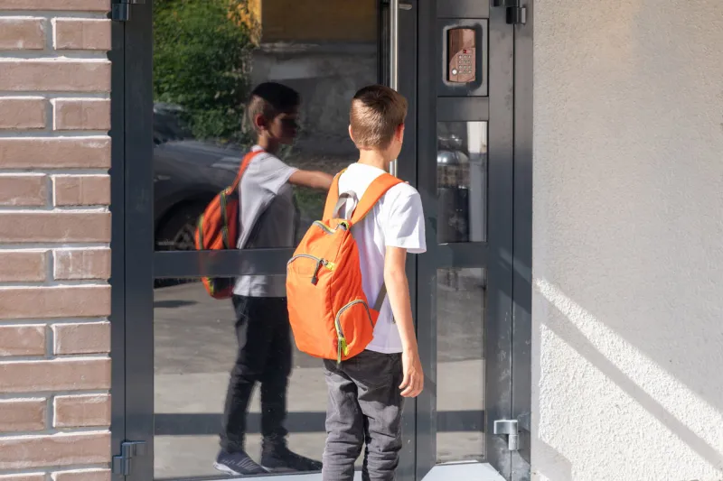 cute boy student with a school backpack opens the door of the house a child returning home after school next to the door of the house back to school concept