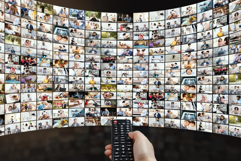 broadcasting and streaming concept person holding remote control, switching channels or choosing movie, watching tv show multimedia and video on demand technology screen with thumbnails