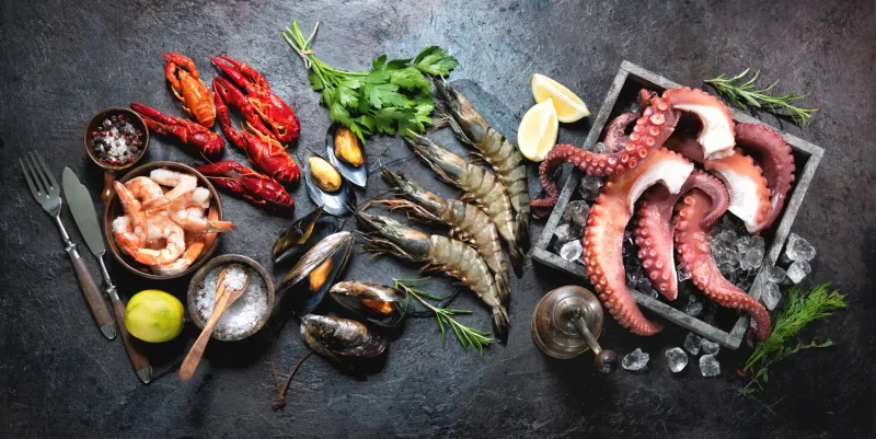 variety of fresh delicious seafood octopus tentacles, black tiger shrimps, king prawn and mussels with fresh herbs and seasoning on black rustic background