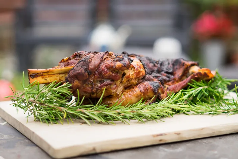slow bbq whole lamb shoulder shot outside shot on a wooden board and a bed of rosemary