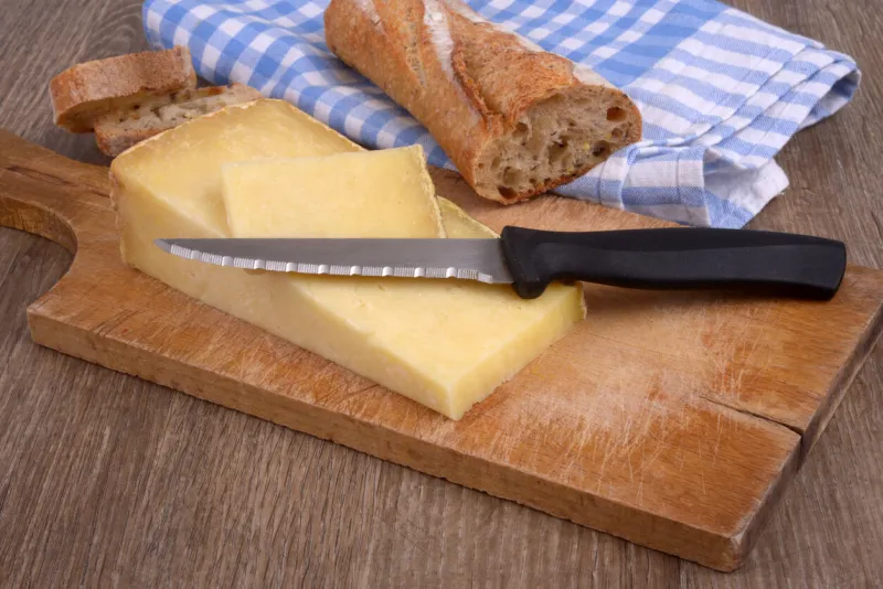 pieces of laguiole cheese with a knife on a cutting board next to a piece of bread in close-up