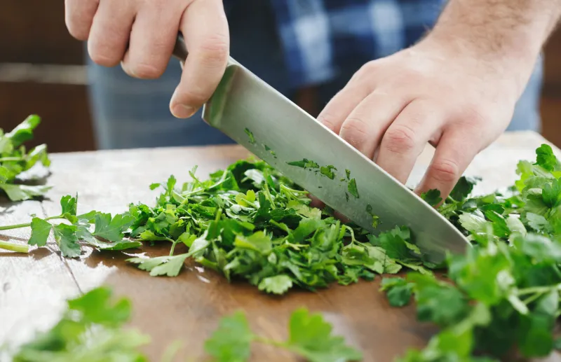man is cooking parsley on wooden table close up