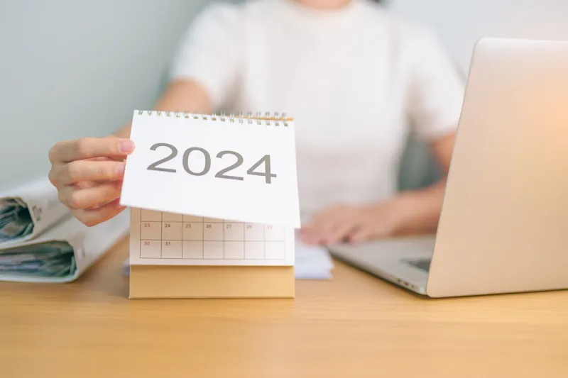 2024 year calendar on table with business woman using laptop computer countdown, happy new year, resolution, goals, plan, action, mission and financial concept