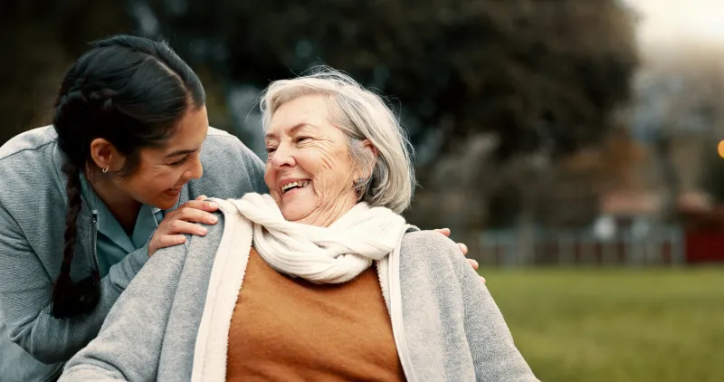 caregiver helping woman with disability in park for support, trust and care in retirement nurse talking to happy senior patient in wheelchair for rehabilitation, therapy and conversation in garden