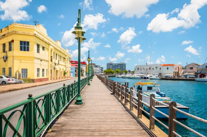 bright image of wooden promenade at the waterfront of bridgetown in barbados colorful building against blue sky with white clouds boats and yachts in the harbor