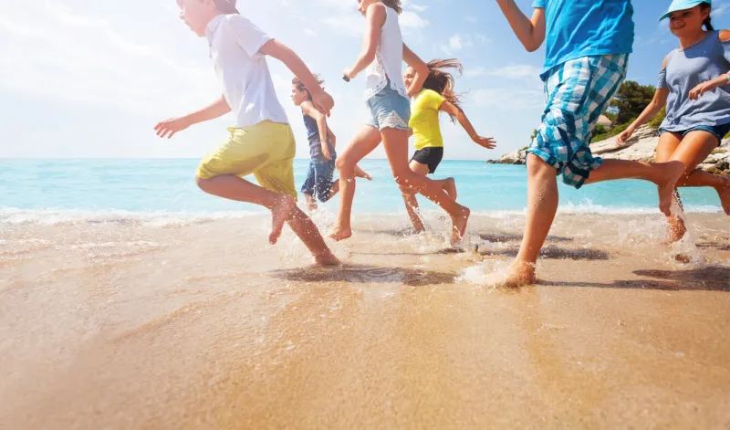 close-up of multiple legs of kids running in shallow sea water with sunlit background