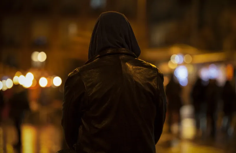 rear view of adult man with hood on street at night