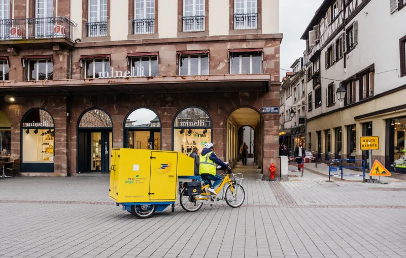 strasbourg  la poste courier delivery riding electric bike with cargo trailer containing letters and parcel