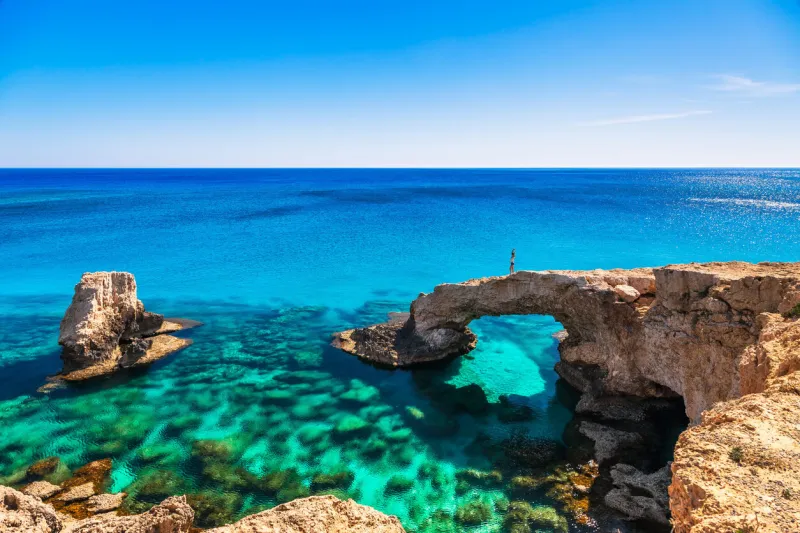 woman on the beautiful natural rock arch near of ayia napa, cavo greco and protaras on cyprus island, mediterranean sea legendary bridge lovers amazing blue green sea and sunny day