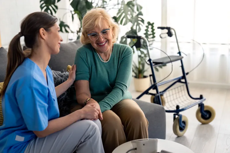 female home care specialist and satisfied elderly woman holding hands while talking and sitting in living room happy senior woman enjoying company of her nurse during regular home visit