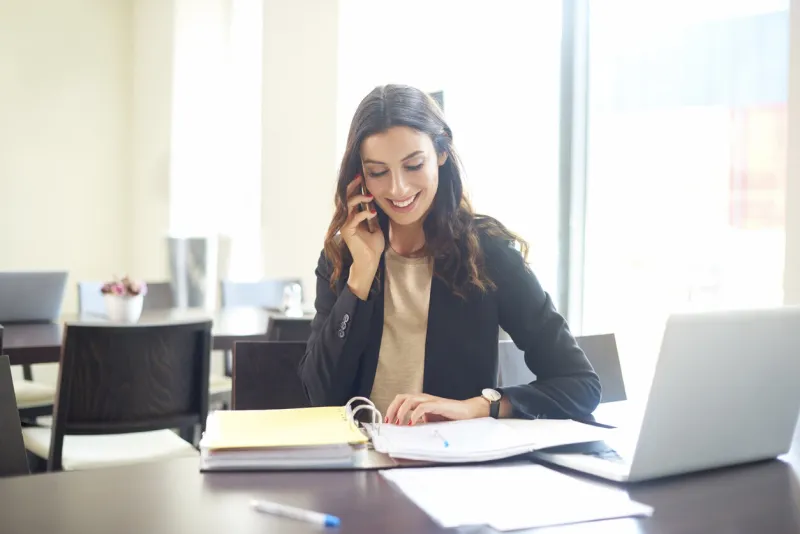 shot of a young businesswoman sitting at office desk in front of laptop and making call while considering the possibilities with her client