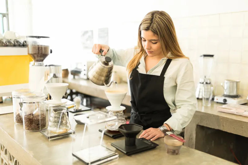 portrait of a pretty female barista pouring water and brewing a cup of coffee at a coffee shop