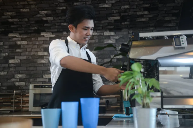 asian male barista using coffee machine in his own cafe in kuala lumpur, malaysia