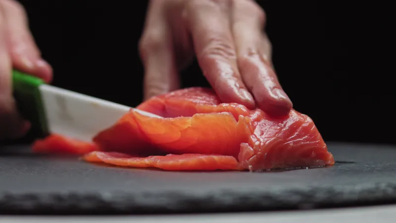 sushi chef slices fresh salmon on the sushi bar chef cutting salmon fillet at professional kitchen closeup chef hands slicing fresh fish slice in slow motion professional man cutting red fish