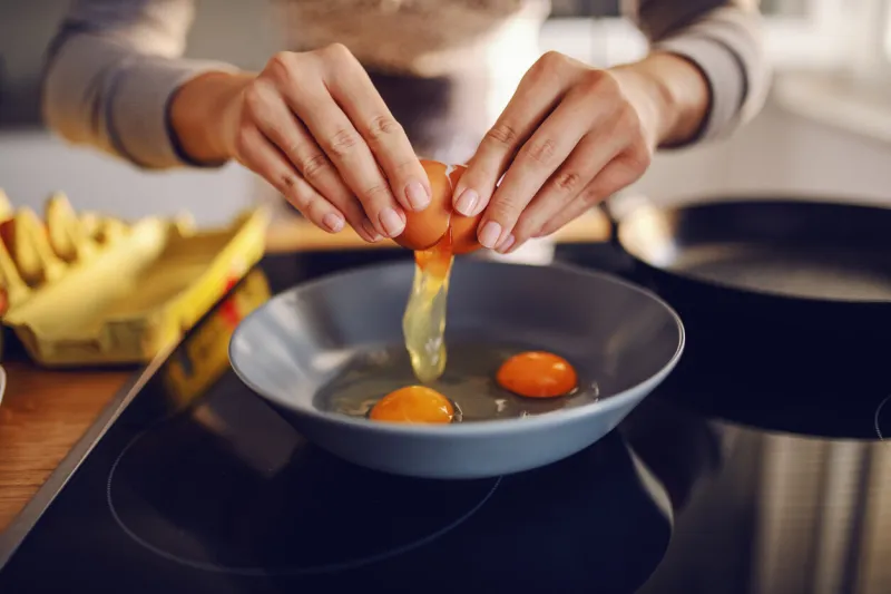 close up of caucasian woman breaking egg and making sunny side up eggs domestic kitchen interior breakfast preparation
