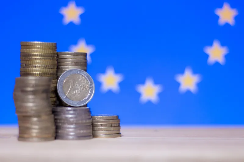 2 euro coin standing on stacks of coins standing in front of flag of european union illustrating concept of economy and finance politics of eu or inflation, savings