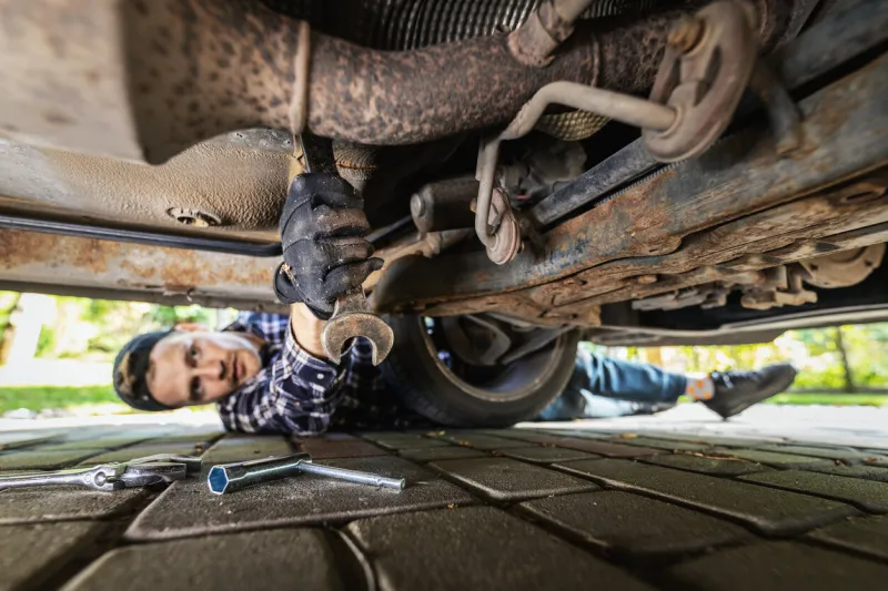 man laying on the ground under the car and repairing engine with wrench