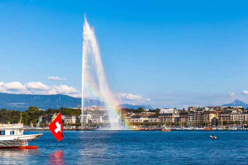 beautiful view of the water jet fountain with rainbow in the lake of geneva and the cityscape of geneva at sunset, switzerland