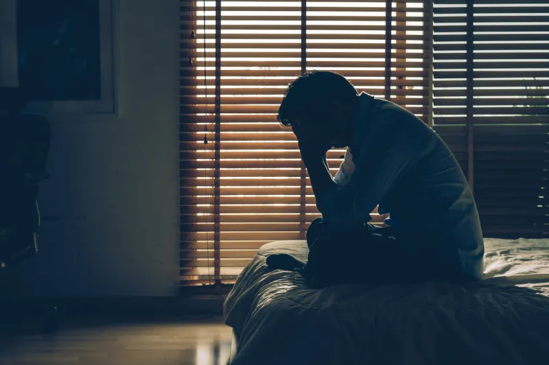 sad businessman sitting head in hands on the bed in the dark bedroom with low light environment, dramatic concept, vintage tone color