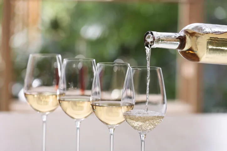 pouring white wine from bottle into glass on blurred background