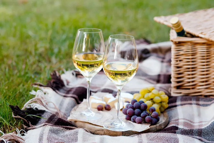 two glasses of white wine and a wooden plate with cheese and grapes served outside