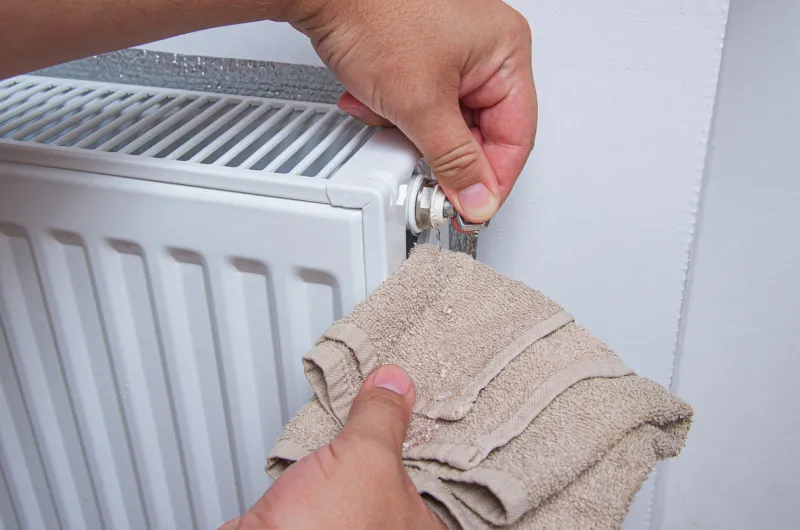 hands with a kitchen towel and key for draining air drains water and air from the heater bleed air valve in heating radiator for adjust heating system