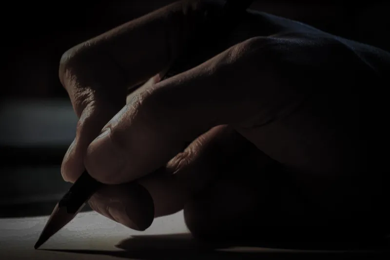hand writing on paper with a pencil, writing at night with minimal light