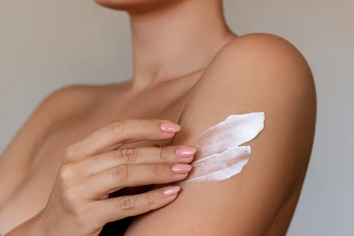 cropped shot of a young tanned woman moisturizing her shoulder with her hand using a cream isolated on a gray background skin care a white thick smear of cream on the female body
