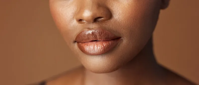 closeup, lips and black woman with beauty, smile and skincare on a brown studio background african person, girl and model with gloss, cosmetics and dermatology with clear skin, smooth and aesthetic