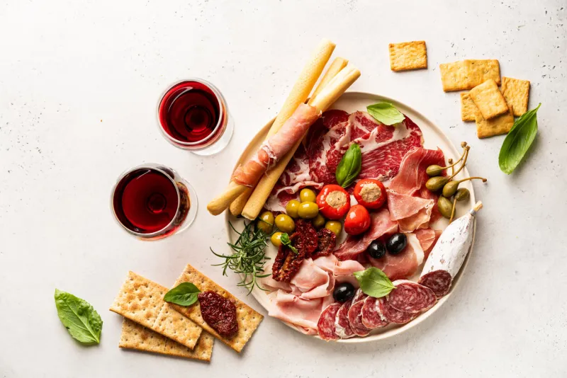 appetizers with differents antipasti, charcuterie, snacks and red wine on white background sausage, ham, tapas, olives and crackers for buffet party top view, flat lay