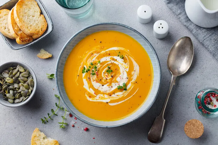 pumpkin and carrot soup with cream on grey stone background top view