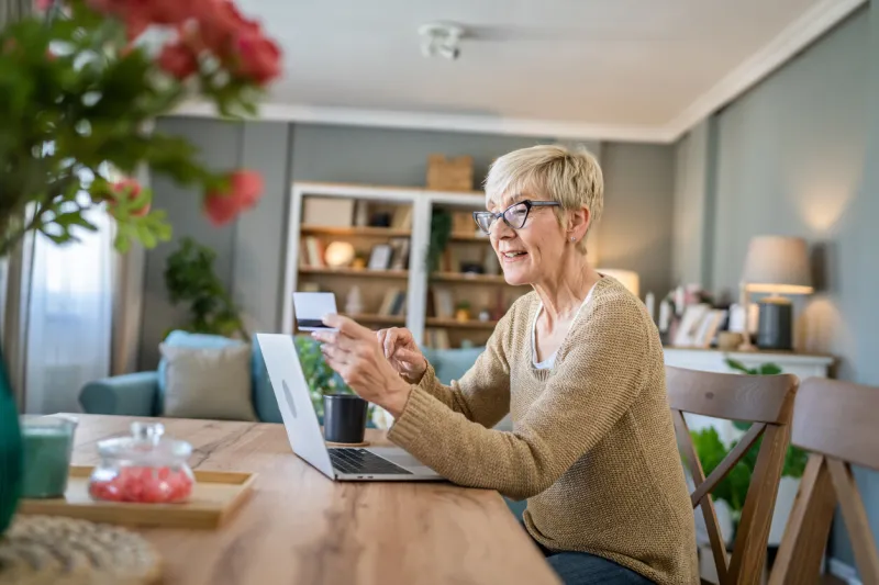 one mature senior woman grandmother sit at home use credit or debit card for online shopping browse internet stores use laptop computer buying stuff real people copy space