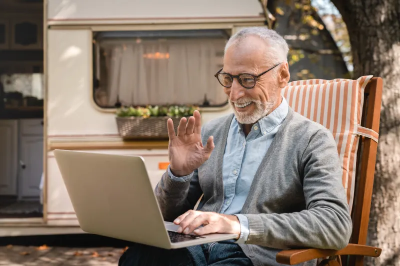 old senior elderly man grandfather using laptop for remote work, having videocall conference online while caravanning by trailer camper van motor home