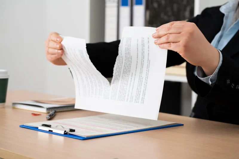 close-up of the hands of a businesswoman tearing up the signed contract document sitting at a desk in the office