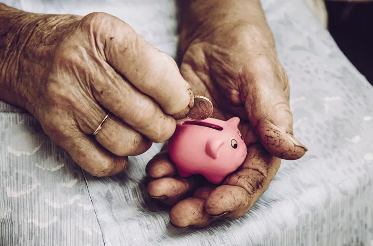 close up view of old dirty rough elderly retired woman hands holding tiny pink piggy bank small pension concept