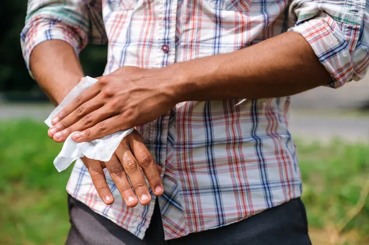 young african american man disinfecting his hands using a wet wipe close up to prevent infection outdoors in park in summer
