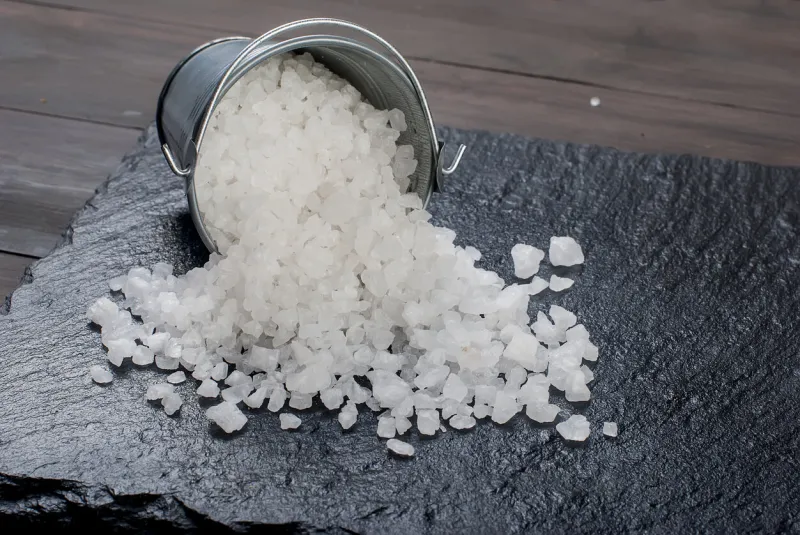 sprinkled sea white salt crystalsin a bucket on a black stone background on a wooden surface