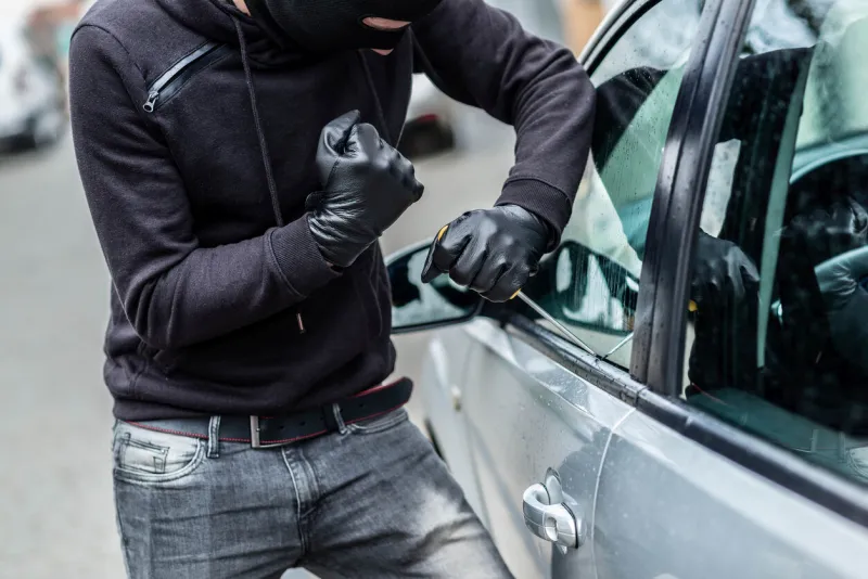 the man dressed in black with a balaclava on his head trying to break into the car he uses a screwdriver car thief, car theft concept