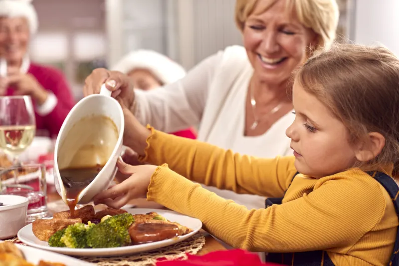 grandmother pouring gravy onto granddaughters food as multi-generation family eat christmas meal
