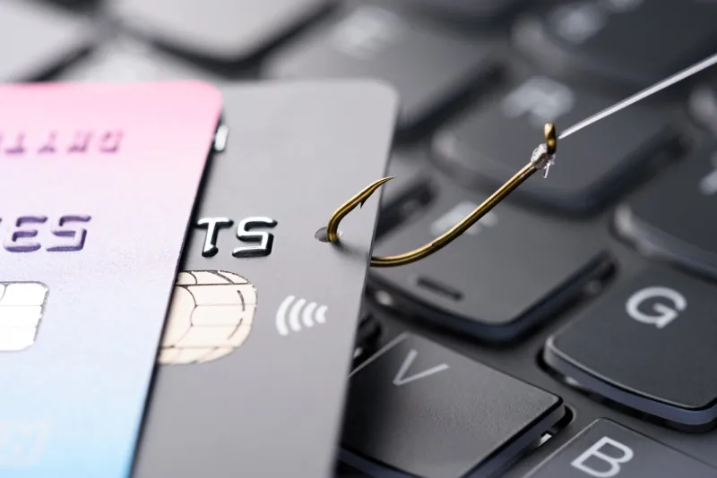 credit card on fishing hook pulled from stack on keyboard, phishing scam data theft concept