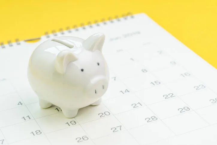 finance, saving money or salary pay day, white piggy bank on white clean calendar on solid yellow background