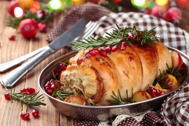 stuffed turkey breast with baked vegetables and spices against holiday lights background